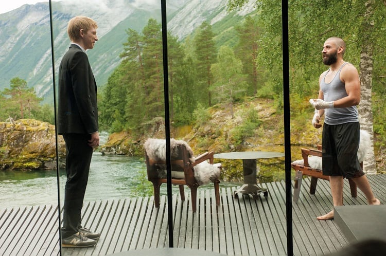 Movie scene inside the Ex Machina house, with wall to ceiling windows opening up to greenery and a river