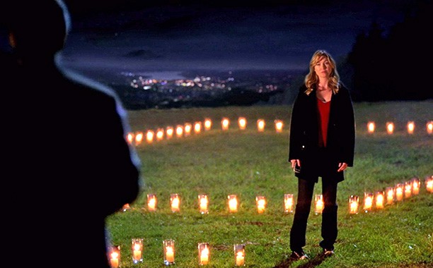 meredith grey standing in front of derek shepherd in the outline of the house made out of candles
