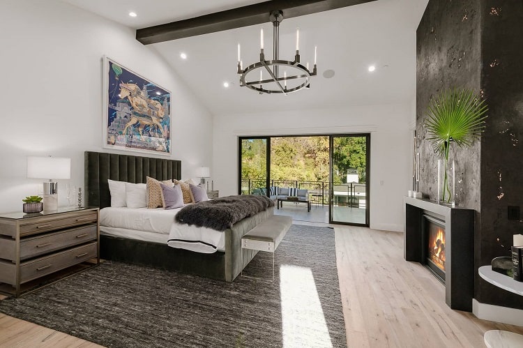 beautiful bedroom with a fireplace, king bed, terrace and beamed ceilings with a wrought-iron chandelier