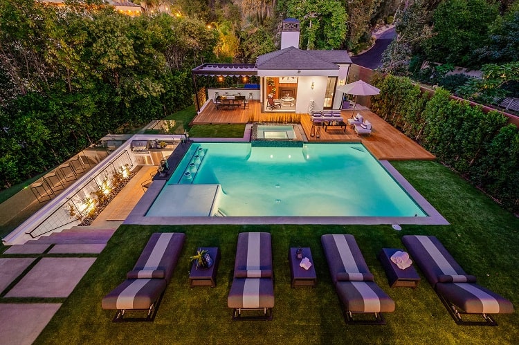 the backyard of Steelo Brim's house with a pool, lounging chairs, pool house, and several seating areas