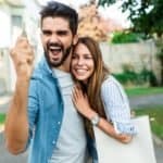 Happy young couple with key in hand standing outside in front of their new home.