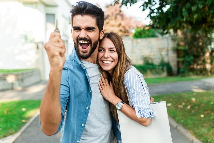 Happy young couple with key in hand standing outside in front of their new home.