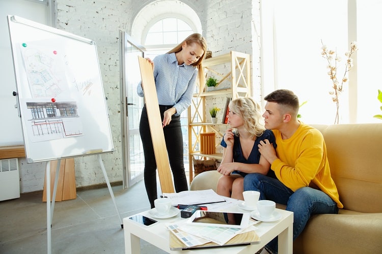 Interior designer working with young couple. Lovely family and professional designer discussing concept of future interior, working with color palette, room drawings in modern office.