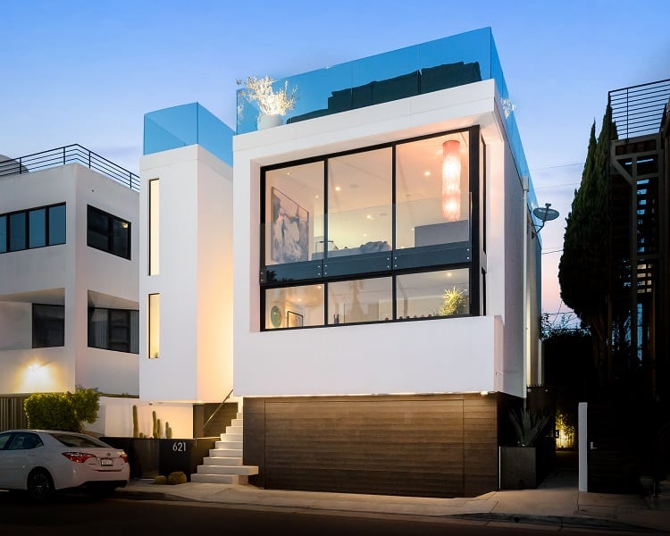 The contemporary home has white exteriors, with tall glass windows and Japanese burnt wood wrapping the garage and lower level