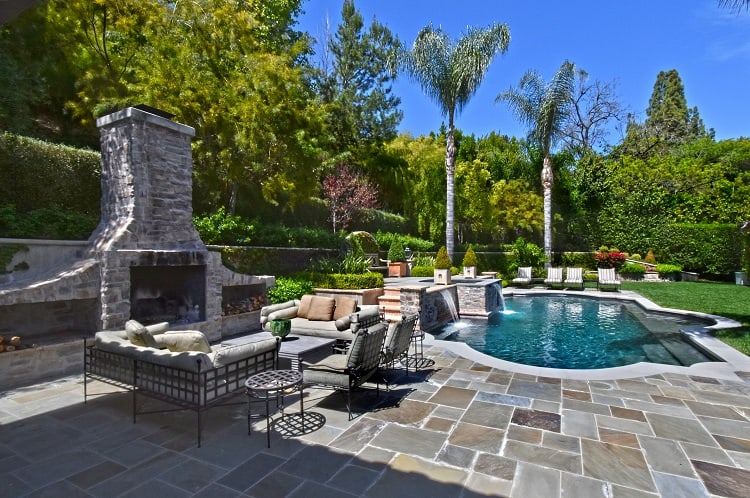 a resort-like backyard with a pool, stone fireplace, and palm trees