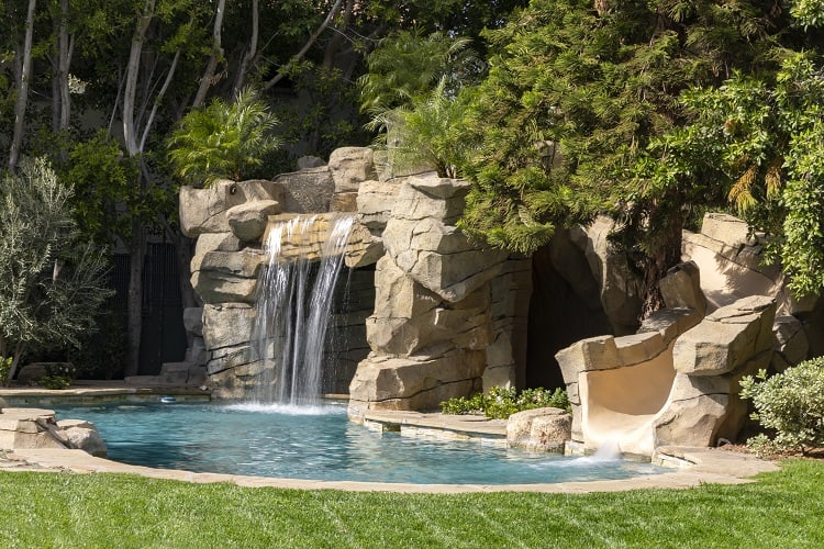 stone waterfall and pool surrounded by landscaping and mature trees