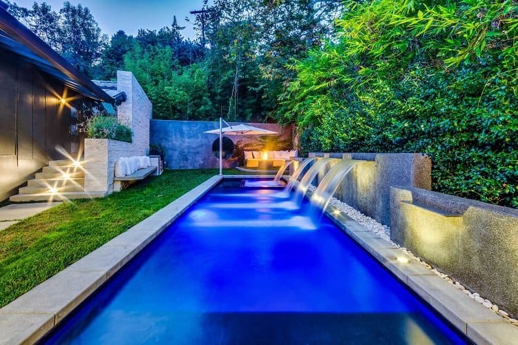 The secluded pool area is surrounded by trees and has waterfalls, a dining deck with firepit and a barbecue island. 