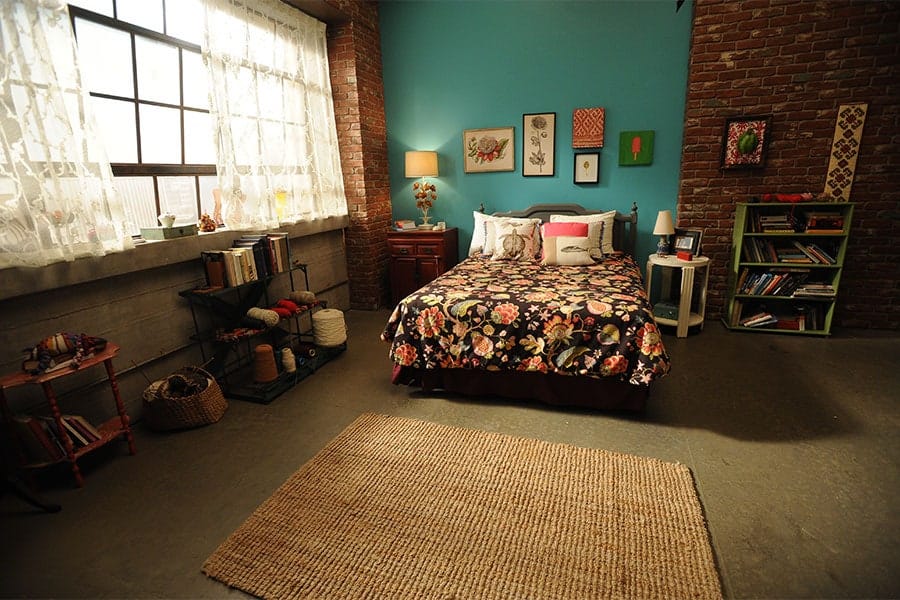 Jess' bedroom in the loft, featuring green walls, a vintage-inspired floral bedspread, and lacy net curtains. 