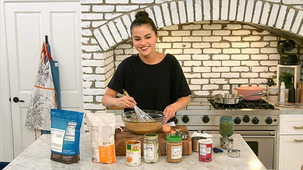 Selena Gomez smiling while whisking in a bowl inside her kitchen