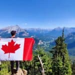 man holding the canadian flag while overlooking the valley and mountains