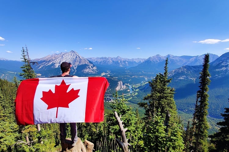 man holding the canadian flag while overlooking the valley and mountains