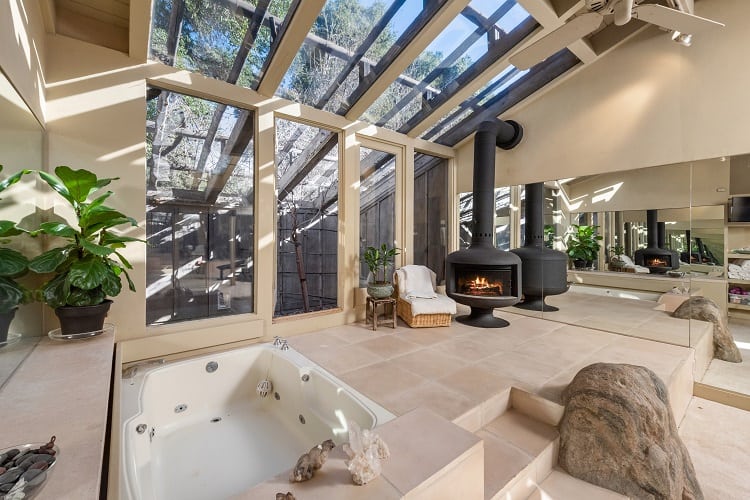 stunning bathroom with glass walls, freestanding fireplace and hot tub