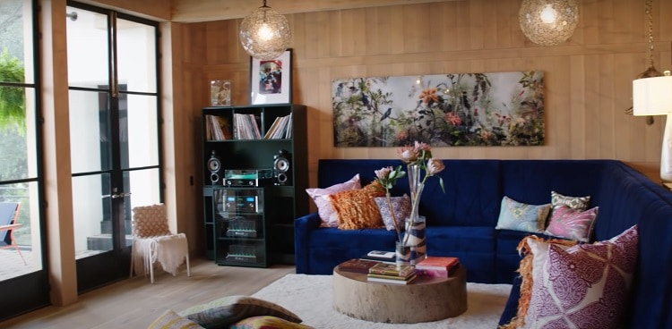 The living room of Jensen Ackles Austin home, with a dark blue velvet couch, colorful pillows, and music equipment