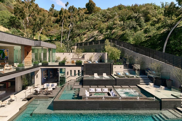 backyard with cascading waterfalls and several seating areas, one at the center of the pool