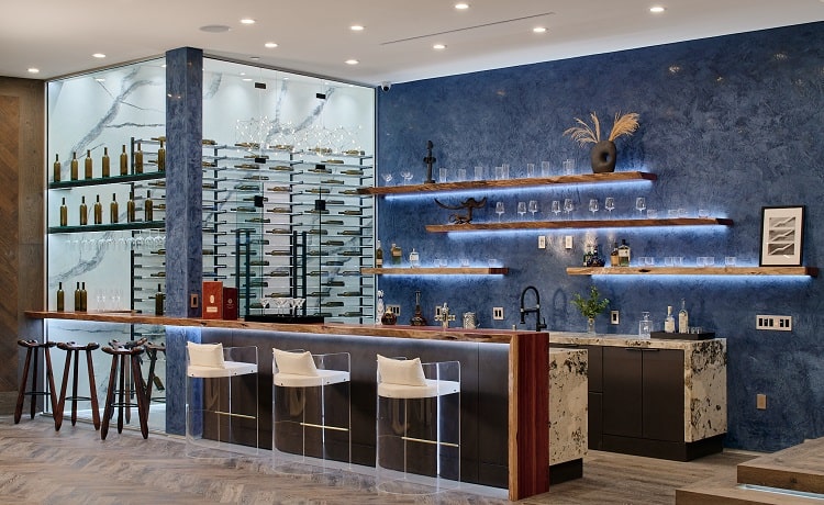 large bar with seating and backlit shelves next to a glass wine cellar with 1000 wine bottles