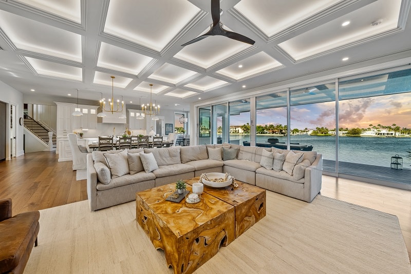 luxury living room with vaulted coffered ceilings and large windows showing the water outside the house