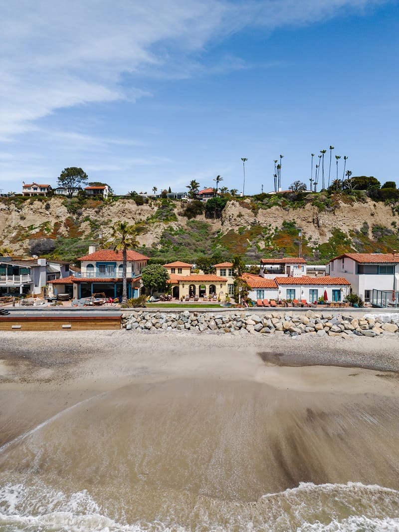 the house seen from the ocean, with the sand and rocks in front