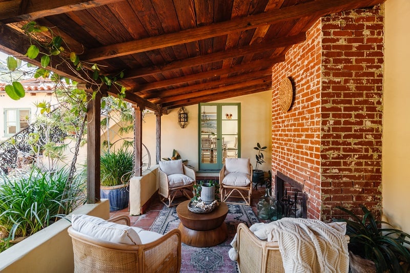 shaded outdoor seating area with four armchairs and a brick wall with fireplace