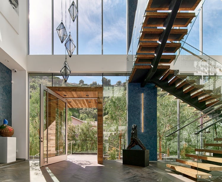 entrance framed by walls of glass next to a floating wood staircase