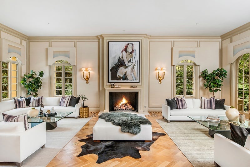 the large living room inside paris hilton's house, with two sets of sofas and a wood burning fireplace in the middle