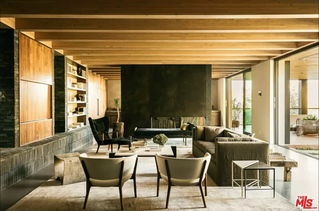 wood-clad interiors anchored by a large concrete fireplace with a sofa and arm chairs in front of it.