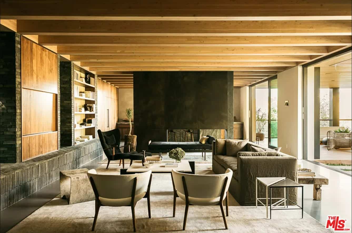 wood-clad interiors anchored by a large concrete fireplace with a sofa and arm chairs in front of it. 