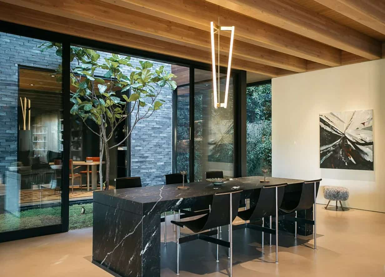 a large black marble counter table with bar stools next to a large window that opens up to a glass-enclosed outdoor area