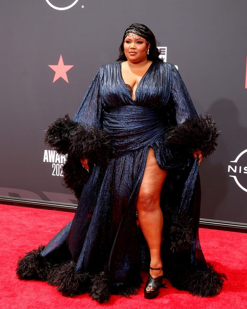 Lizzo on the red carpet at the 2022 BET Awards wearing a lavish black gown with feather accents and a thigh slit 