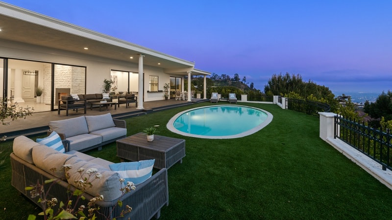 exterior of a Hollywood Regency-style residence with a round pool in front and unobstructed views of Los Angeles and the ocean