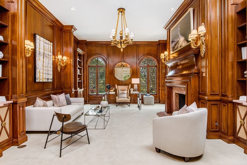 wood-paneled study with sofa, armchairs, desk and a fireplace