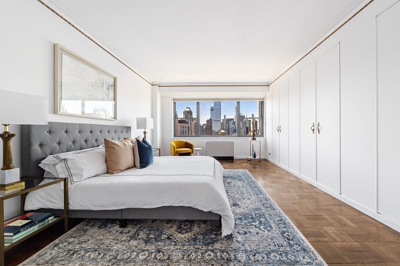 large bedroom with a king bed and windows showing New York skyscrapers