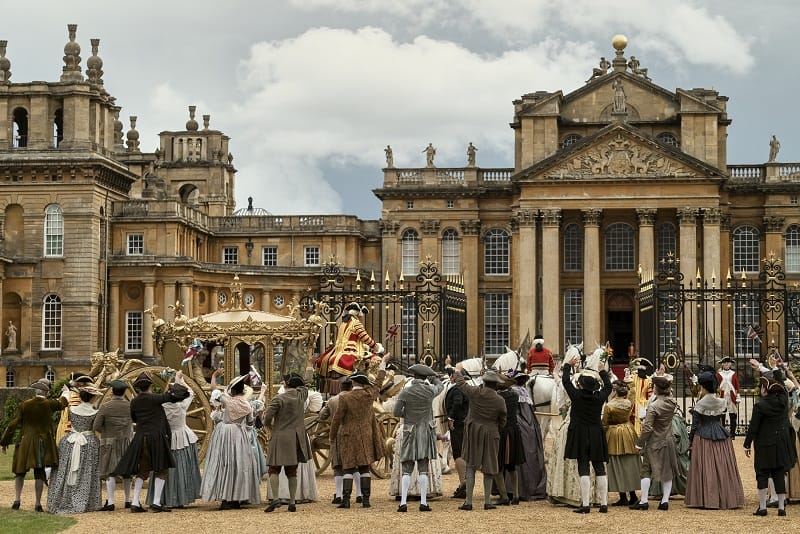 Corey Mylchreest as Young King George in Queen Charlotte: A Bridgerton Story, in a golden carriage in front of the castle, with a crowd surrounding him