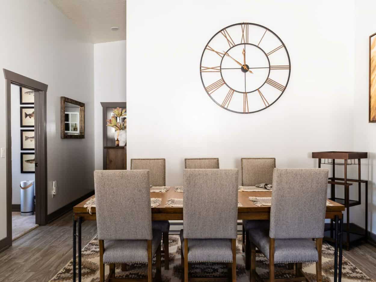 dining room with grey fabric chairs and a large clock on the wall showing roman numbers