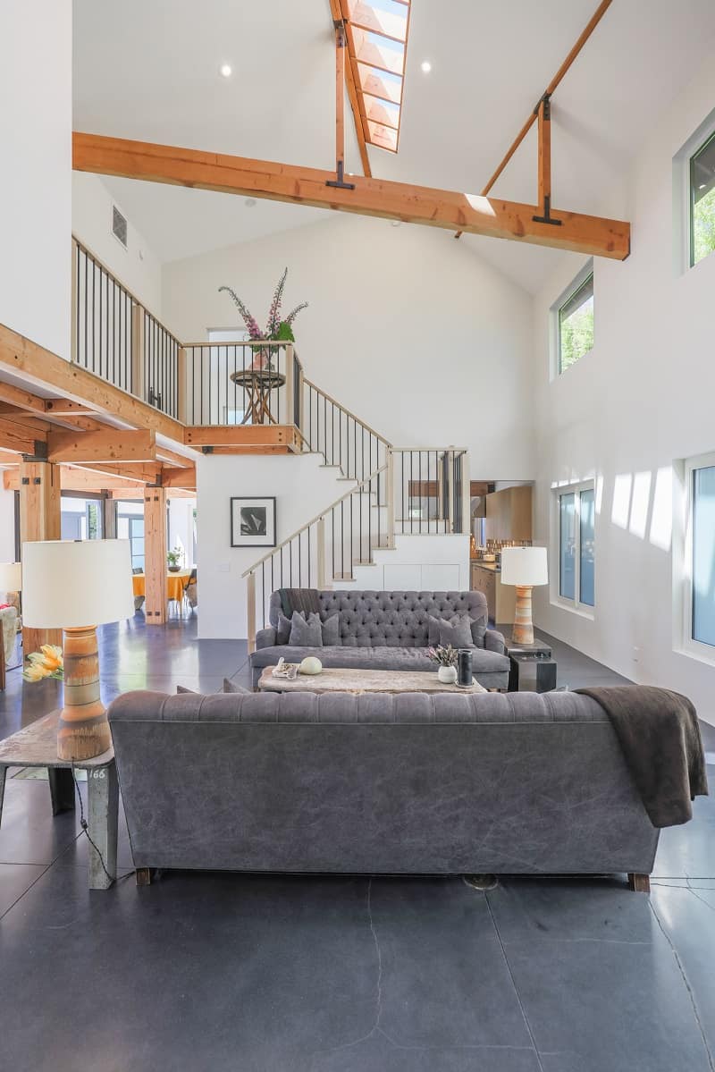 bright living room with wood beams, two-story ceiling, two sofas, and a staircase leading to the second floor