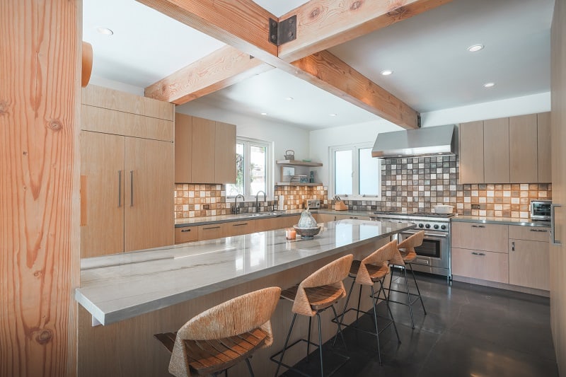 warm wood kitchen with marble counter, tile backsplash, and wooden beams 