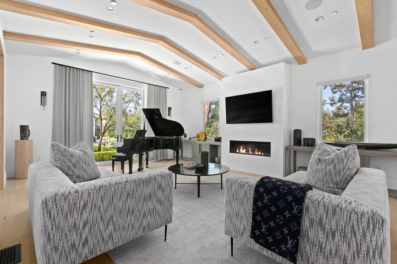 living room with beamed ceilings, black piano, fireplace with TV mounted above it and sofa with coffee table