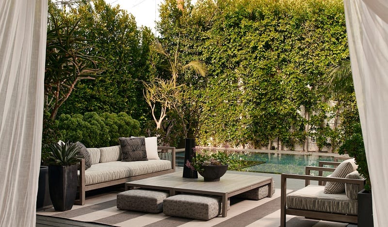 outdoor seating (couches, chairs and large coffee table) next to the pool, surrounded by greenery