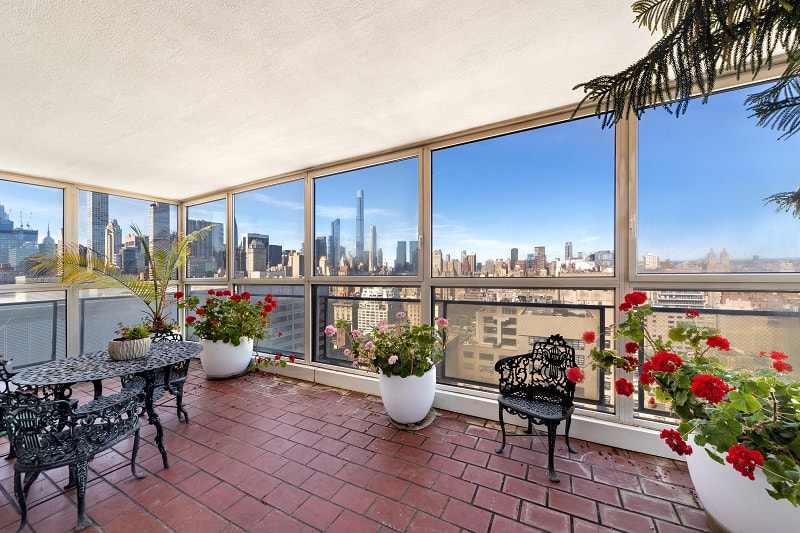 solarium with potted plants, forged iron chairs and table, and large windows overlooking the New York skyline