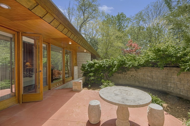 open doors leading out to a patio with stone table and chairs, with landscaping behind it