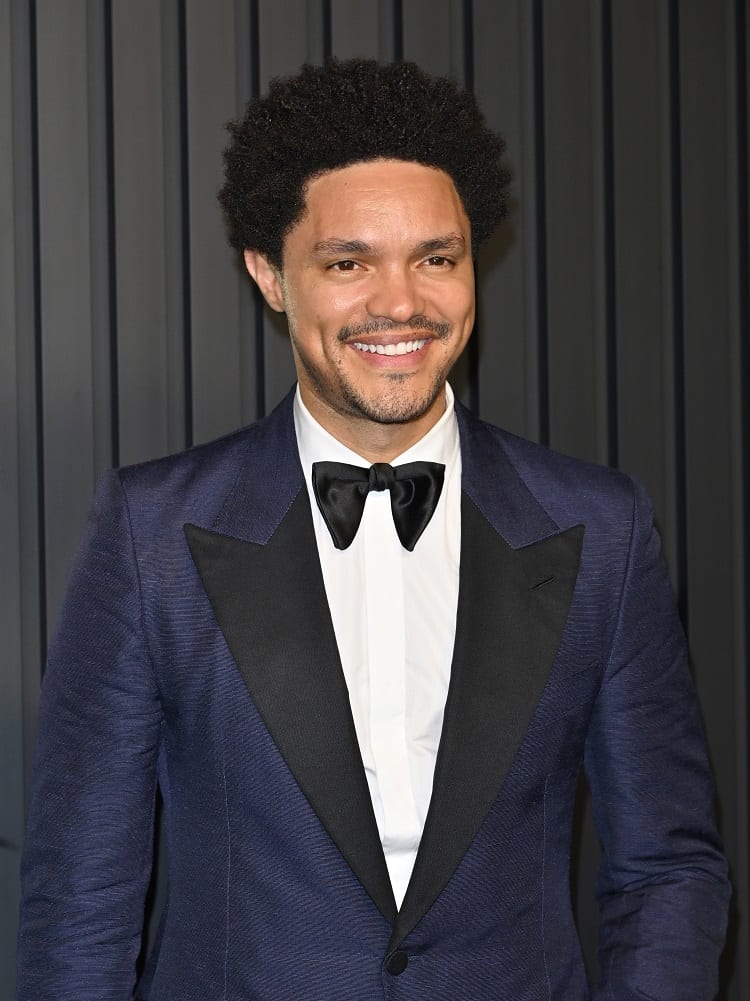 Trevor Noah on the red carpet wearing a dark blue suit and a black bow-tie