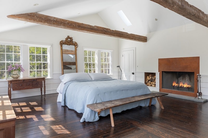 The primary bedroom with beamed ceilings and a fireplace inside the Floating Farmhouse in Eldred, NY.