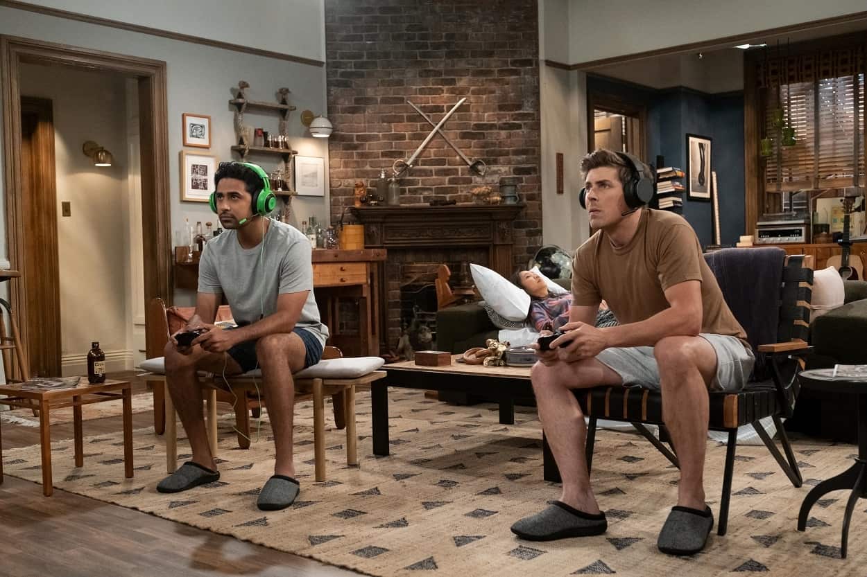 Sid (Suraj Sharma) and Jesse (Chris Lowell) playing video games in their apartment on How I Met Your Mother, with the swords from Ted and Marshall's apartment in the background. 