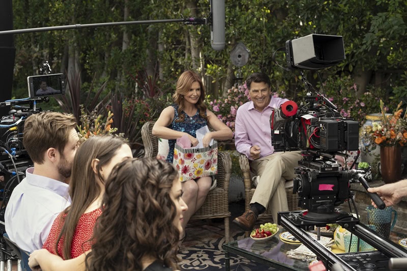 A behind-the-scenes shot showing the main characters in the TV series The Baxters gathered around in the backyard, opening presents with the filming cameras in view. 