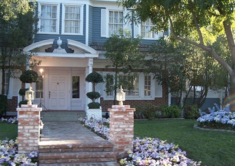 Exterior of Bree Van De Kamp's house on Desperate Housewives, a blue colonial with an arched entrance and many flowers planted in front.