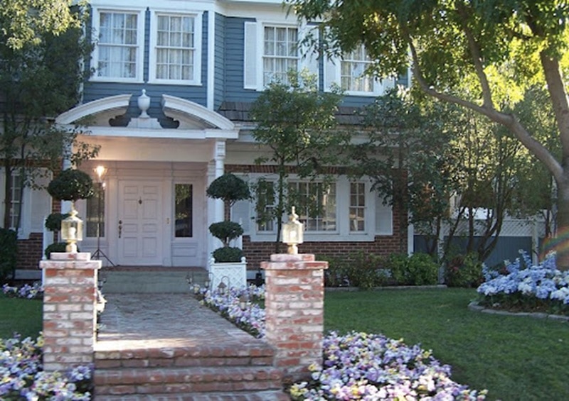 Exterior of Bree Van De Kamp's house on Desperate Housewives, a blue colonial with an arched entrance and many flowers planted in front. 