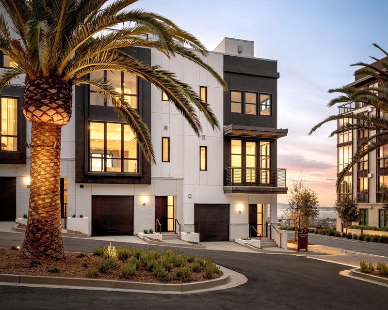 A closer view of two of the townhomes, with light on inside, and the water slightly visible in the background.