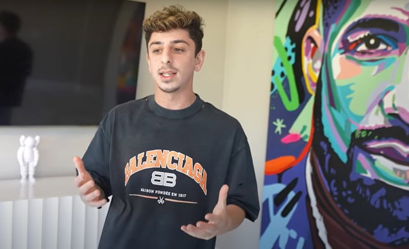 Faze Rug explaining something to the camera with a big art piece behind him.