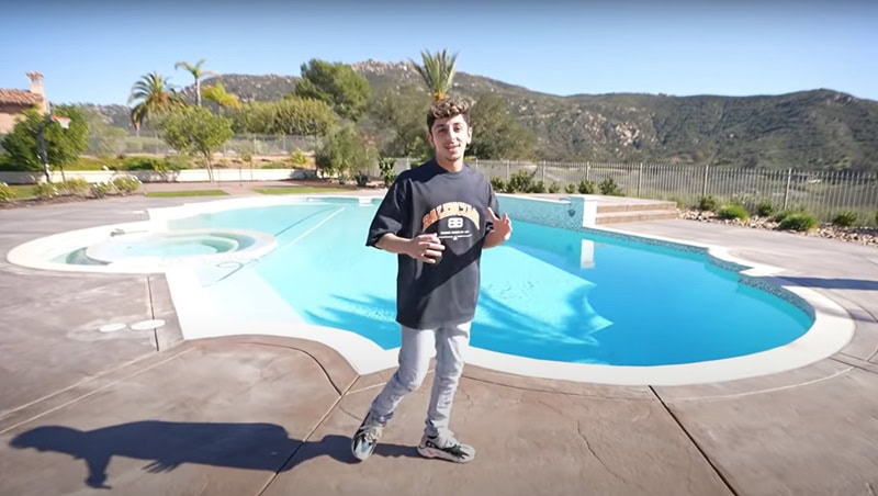 Faze Rug sitting in his backyard, showing viewers his pool area with the mountains in the background.