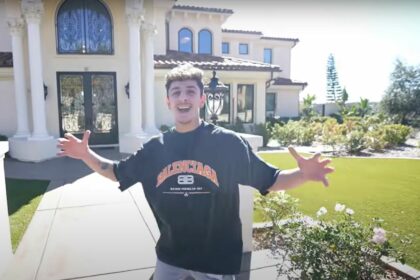 YouTube creator FaZe Rug standing in front of his California mansion, with arms extended, inviting viewers in.