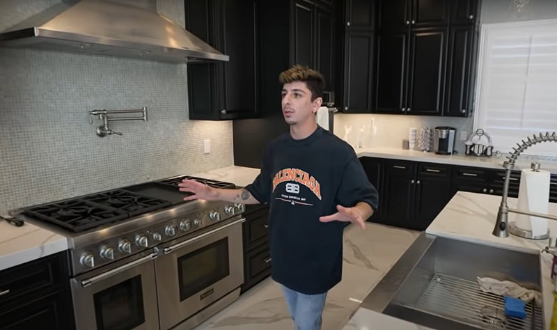 Faze Rug touring the kitchen of his house with black cabinets, a double oven and stove, and a stove hood above